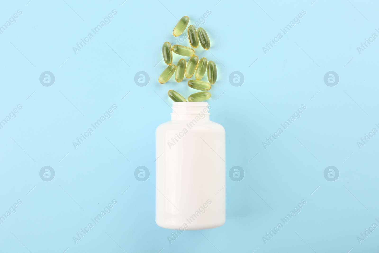 Photo of Bottle and vitamin capsules on light blue background, top view