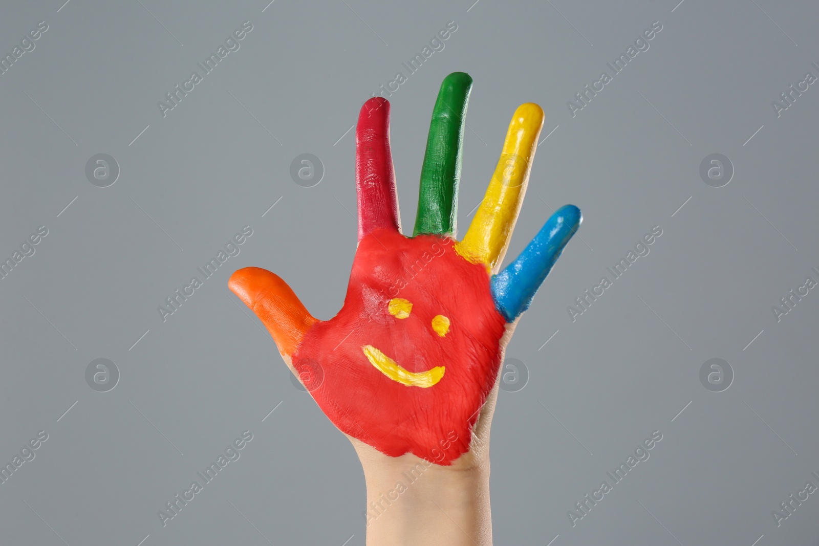 Photo of Kid with smiling face drawn on palm against grey background, closeup