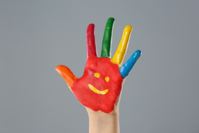 Photo of Kid with smiling face drawn on palm against grey background, closeup