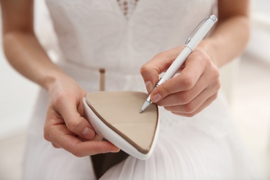 Photo of Young bride writing on her shoe indoors, closeup. Wedding superstition