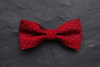 Stylish burgundy bow tie with polka dot pattern on black table, top view