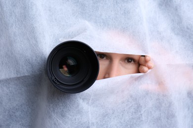 Photo of Hidden woman with camera spying through hole in white fabric, closeup