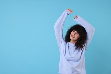 Happy young woman in stylish warm sweater on light blue background, space for text