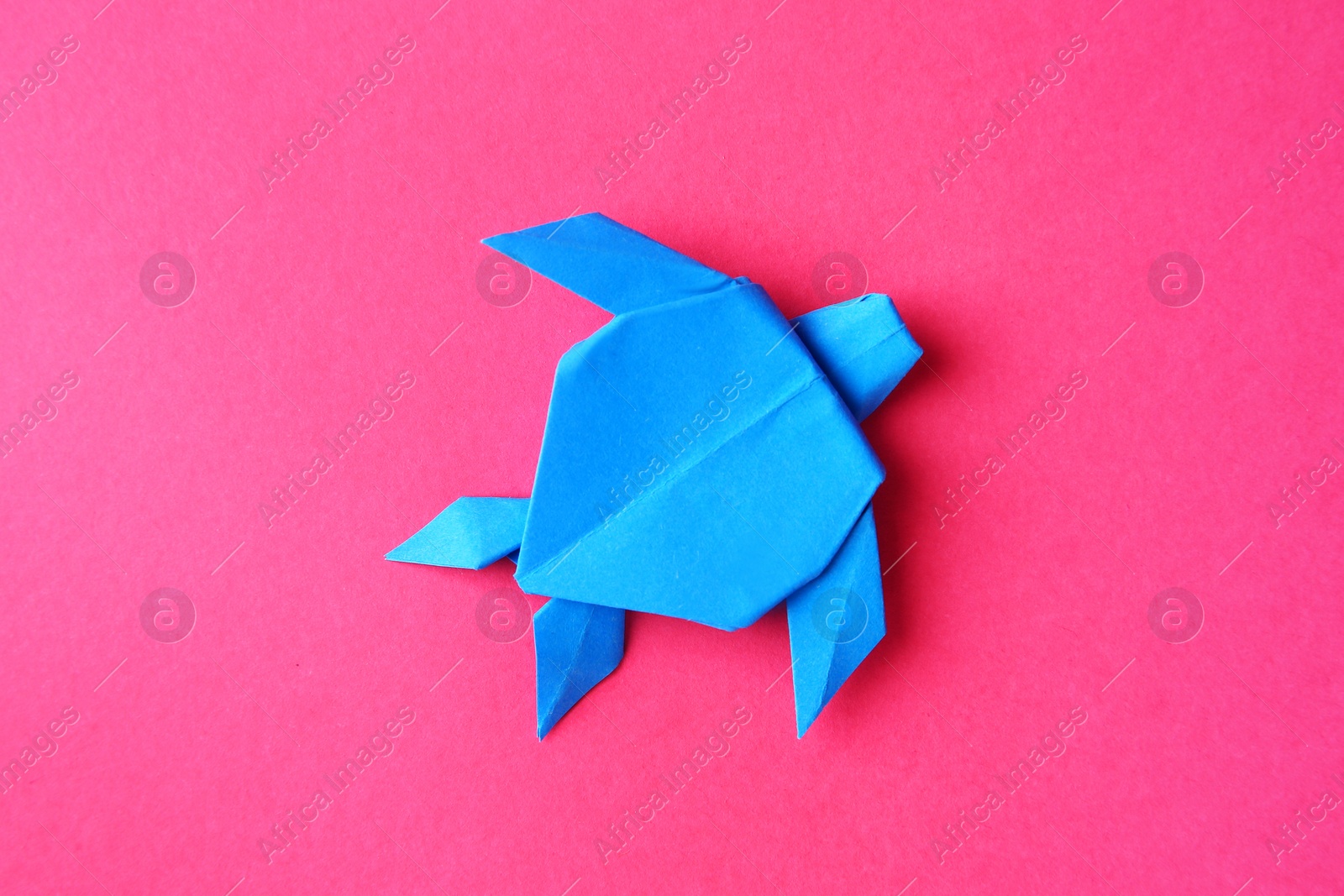 Photo of Origami art. Handmade light blue paper turtle on pink background, top view