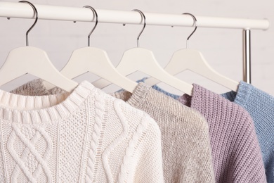 Photo of Collection of warm sweaters hanging on rack against white background, closeup