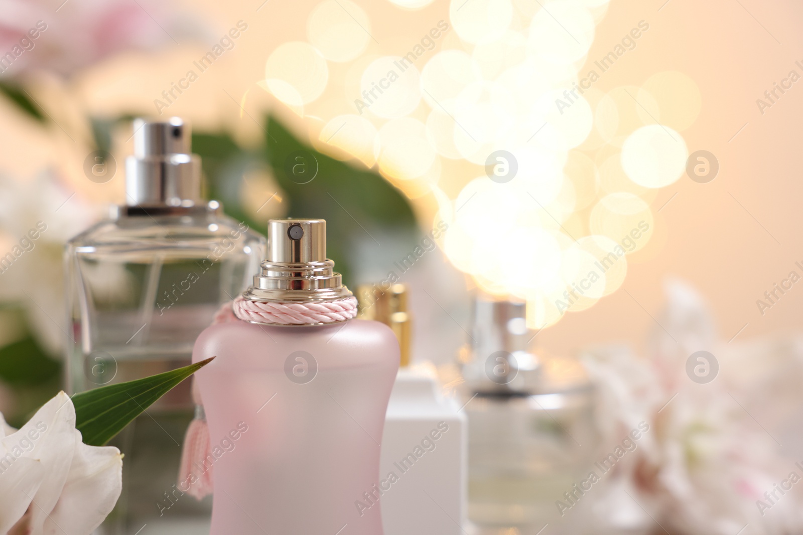 Photo of Bottles of perfume against beautiful lily flowers and blurred lights, closeup. Space for text