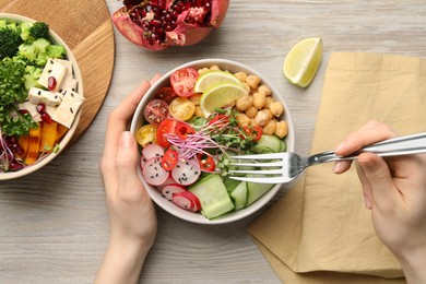 Woman eating dish of salad with vegetables at white wooden table, top view. Vegan diet