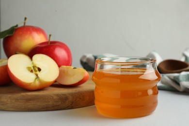Photo of Sweet honey and fresh apples on white table, selective focus. Space for text