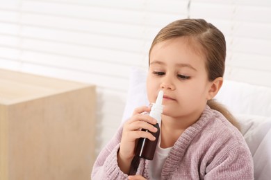 Photo of Little girl using nasal spray indoors, space for text