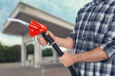Man holding fuel nozzle near gas station, closeup