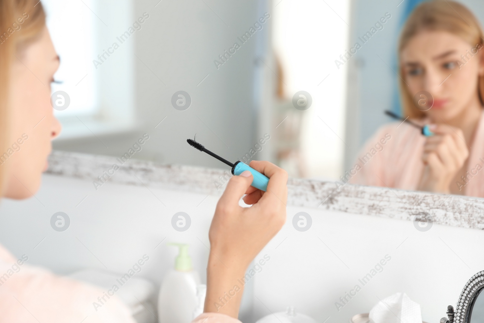 Photo of Young woman holding mascara brush with fallen eyelashes indoors