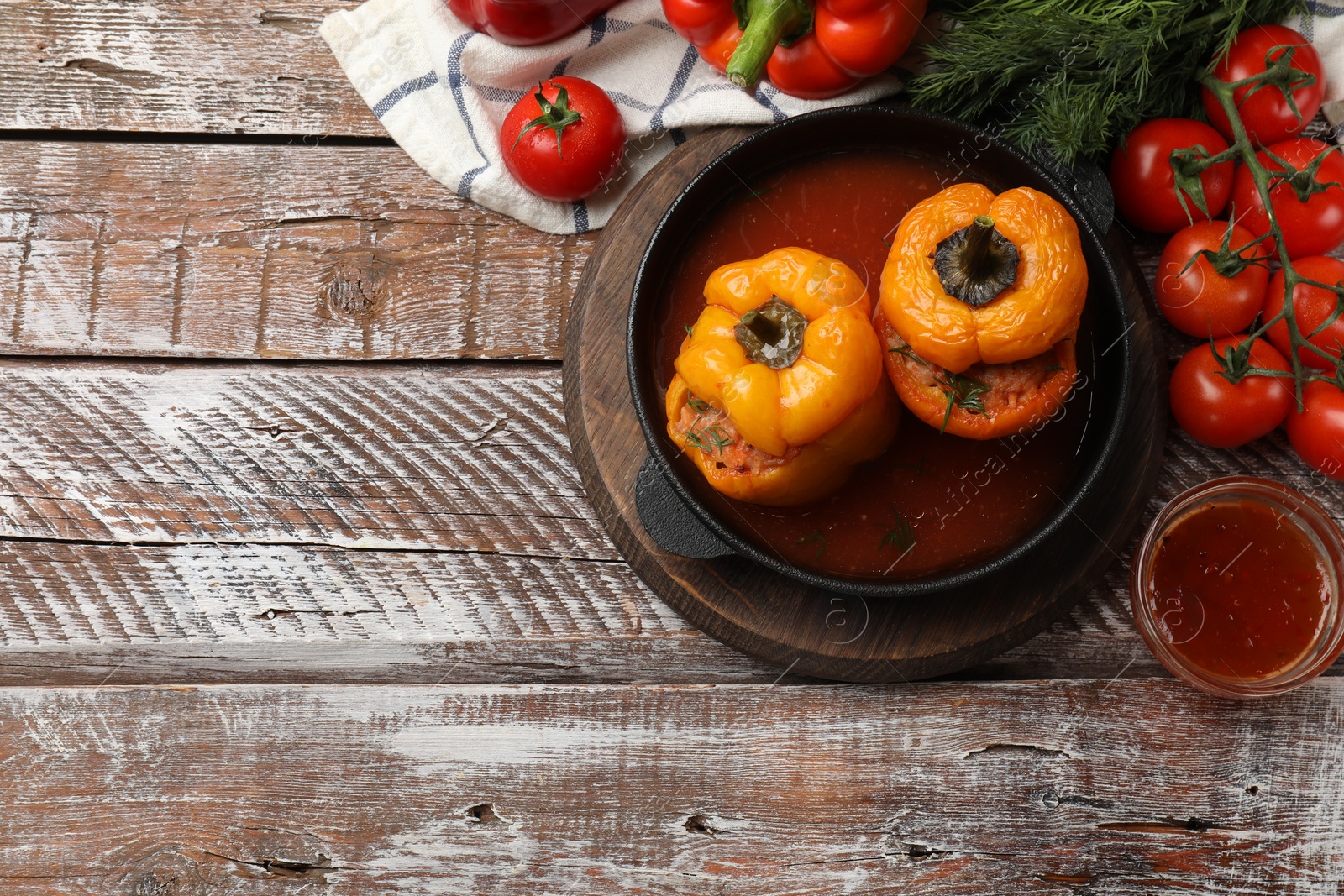 Photo of Tasty stuffed peppers in pan, sauce and products on wooden rustic table, flat lay. Space for text