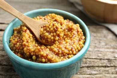 Photo of Whole grain mustard in bowl and spoon on wooden table, closeup