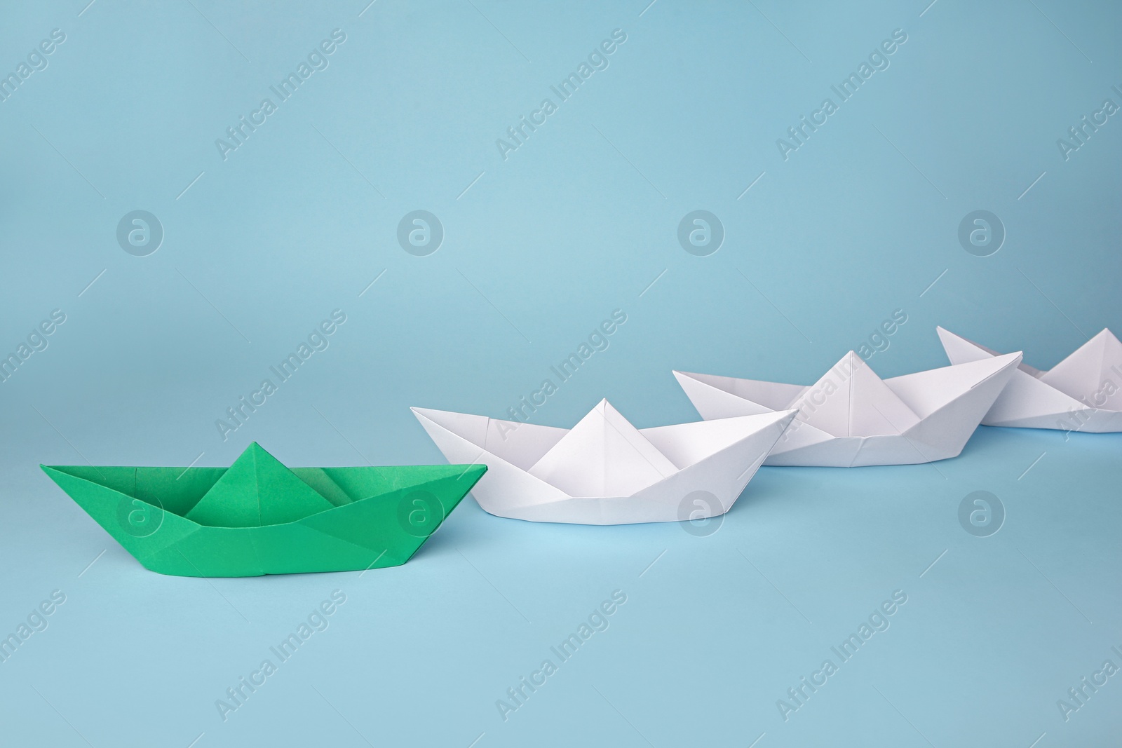 Photo of Group of paper boats following green one on light blue background. Leadership concept