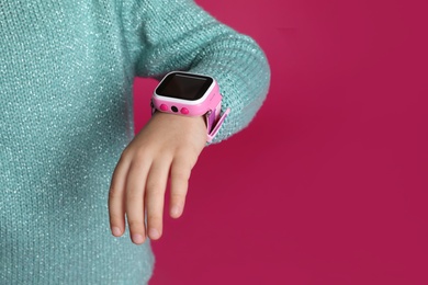 Photo of Little girl with smart watch on pink background, closeup. Space for text