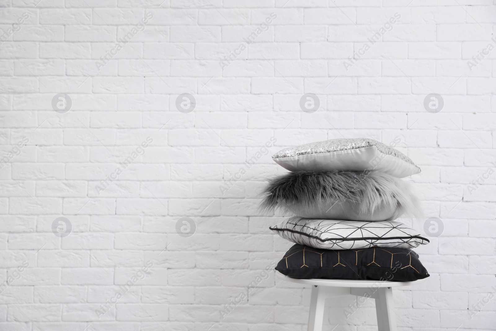 Photo of Many different pillows on chair near brick wall with space for text