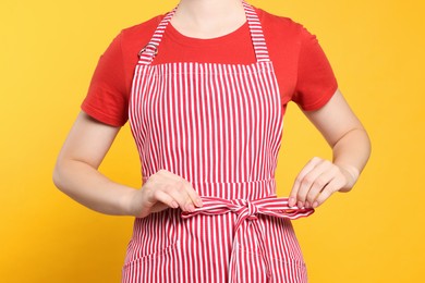 Photo of Woman in clean striped apron on orange background, closeup
