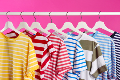 Photo of Colorful clothes on hangers against pink background