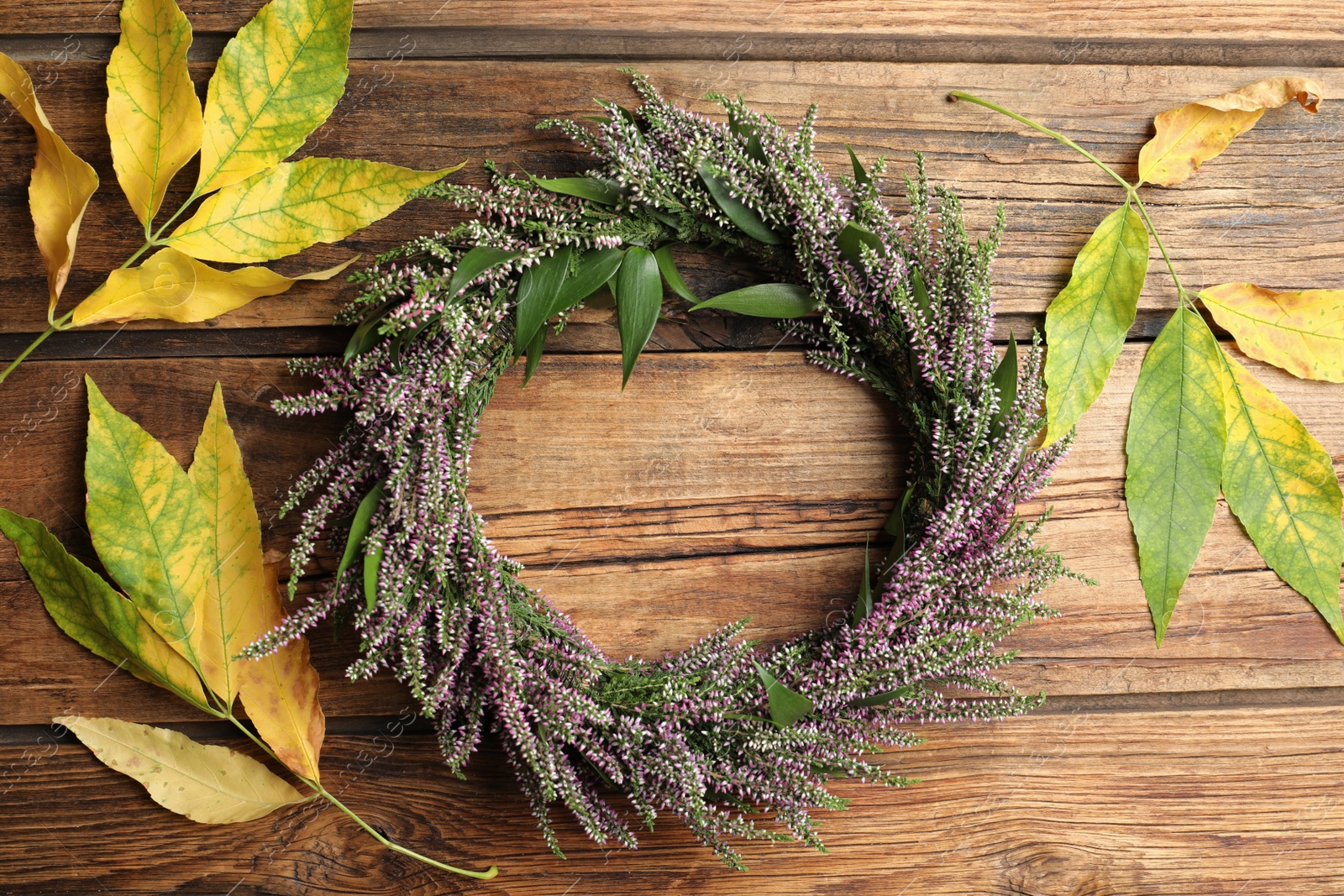 Photo of Beautiful autumnal wreath with heather flowers and leaves on wooden background, flat lay. Space for text
