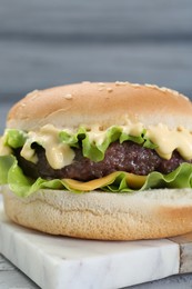 Photo of Delicious cheeseburger with lettuce, sauce and patty on table, closeup