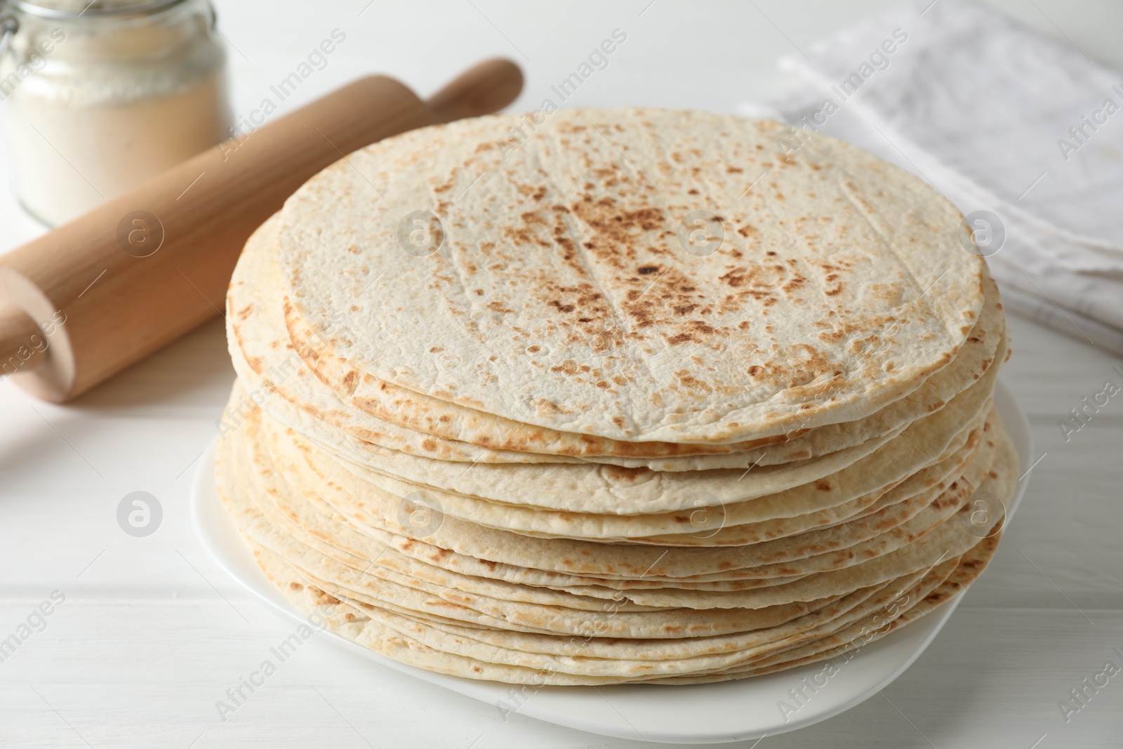 Photo of Stack of tasty homemade tortillas and rolling pin on white wooden table