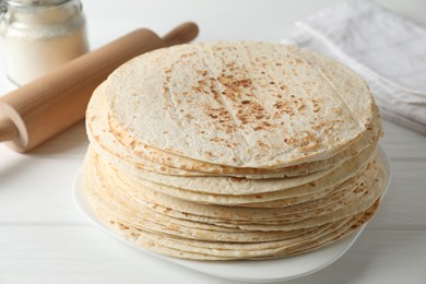 Stack of tasty homemade tortillas and rolling pin on white wooden table