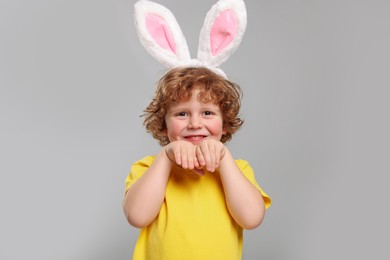 Photo of Portrait of happy boy wearing cute bunny ears headband on light grey background. Easter celebration