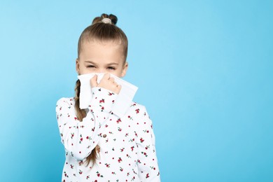 Photo of Sick girl blowing nose in tissue on turquoise background, space for text. Cold symptoms