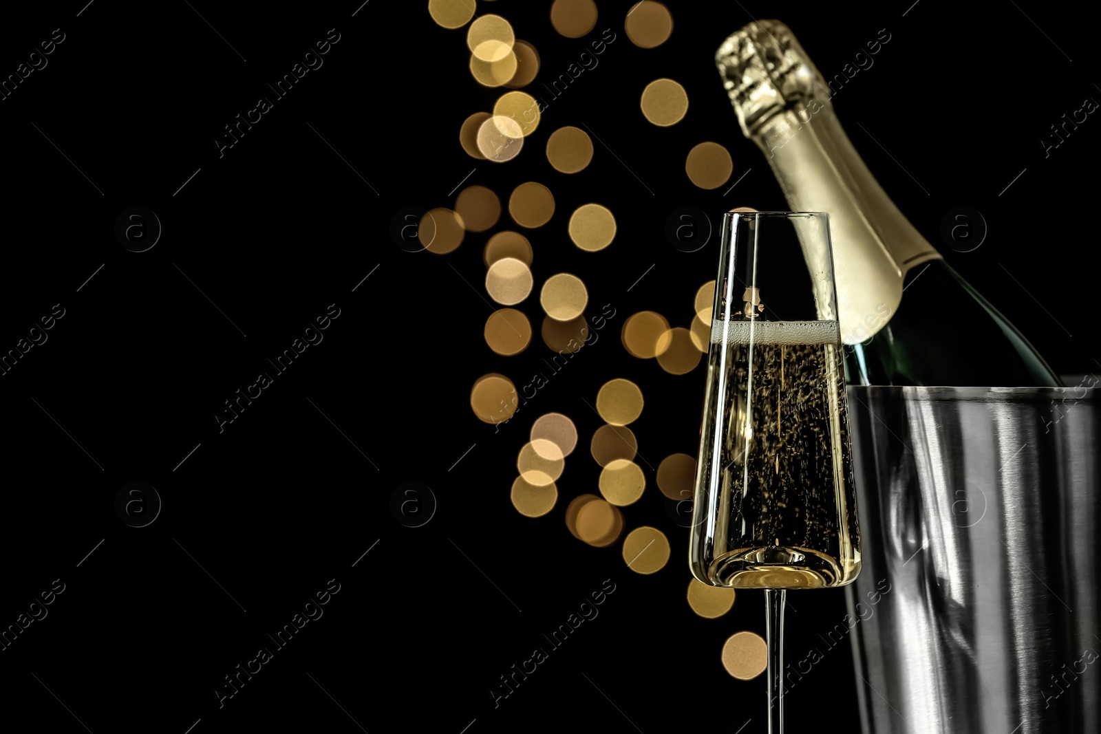 Photo of Glass of champagne near bucket with bottle against blurred lights, space for text