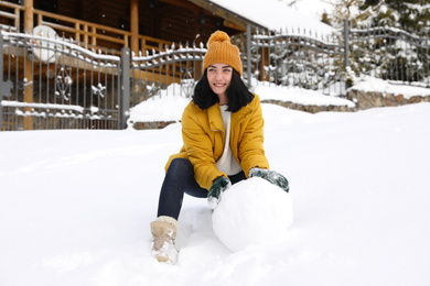 Photo of Happy woman making ball for snowman outdoors. Winter vacation