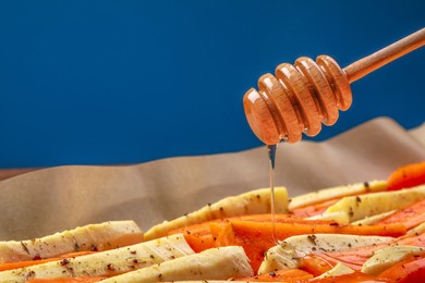 Pouring honey onto slices of parsnip and carrot against blue background, closeup