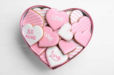 Delicious heart shaped cookies in box on white wooden table, top view. Valentine's Day