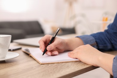 Young woman writing in notebook at wooden table, closeup