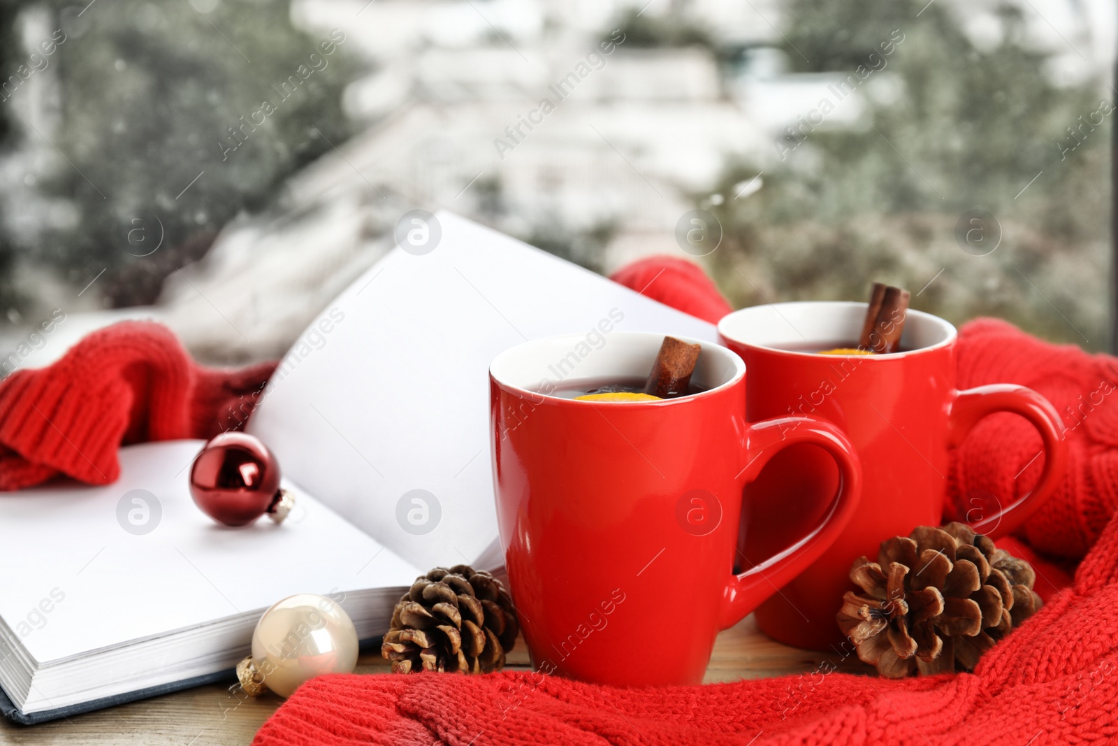 Photo of Cups of hot winter drink with knitted sweater on window sill indoors