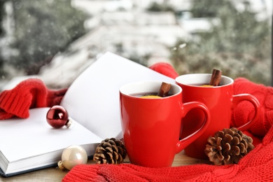 Photo of Cups of hot winter drink with knitted sweater on window sill indoors