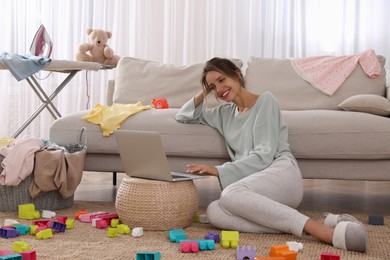Photo of Young mother working with laptop on floor in messy room