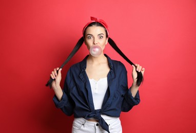 Photo of Fashionable young woman in pin up outfit blowing bubblegum on red background