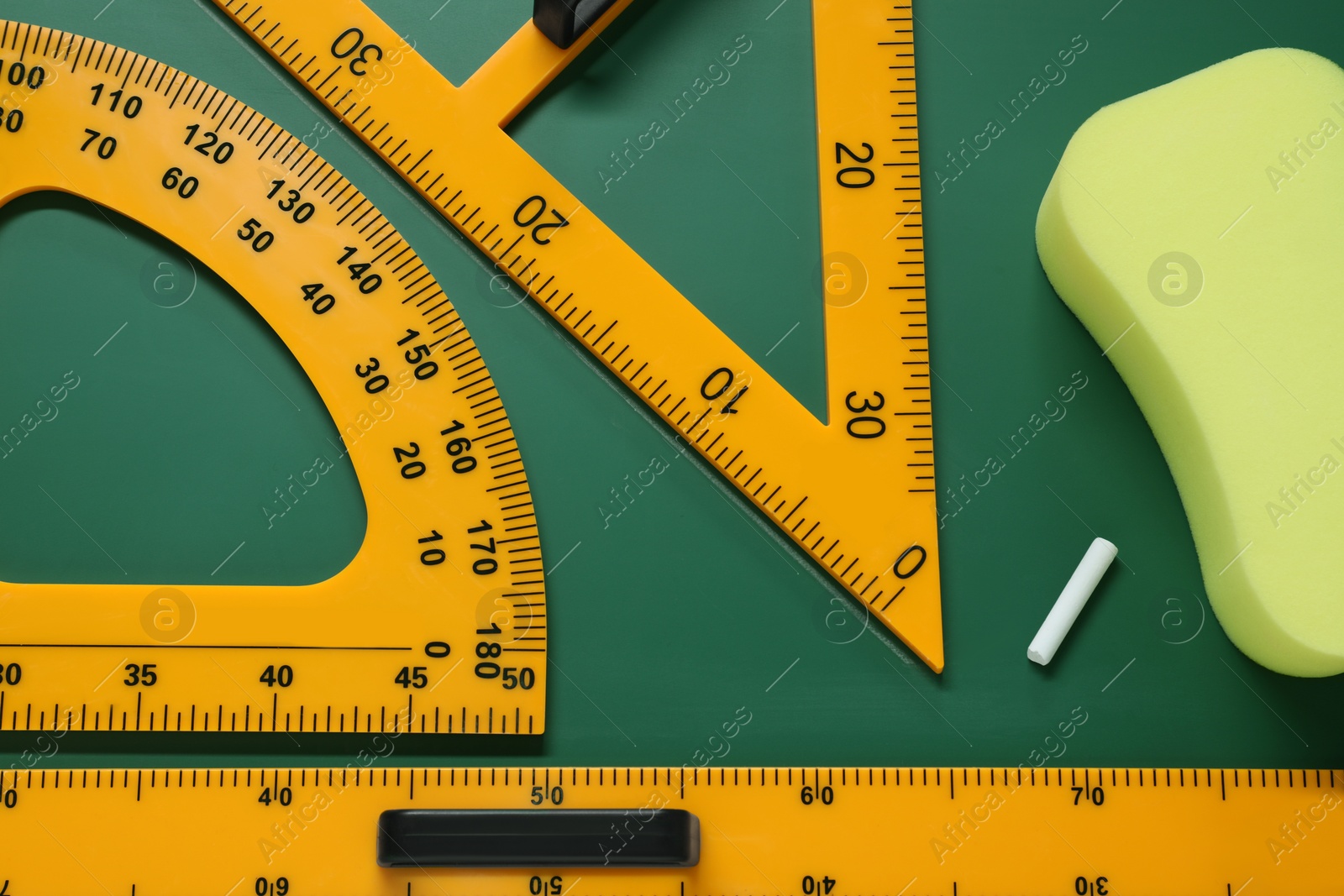 Photo of Protractor, triangle, ruler and sponge on green chalkboard, flat lay