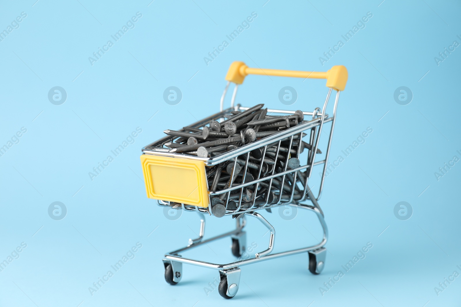 Photo of Metal nails in shopping cart on light blue background