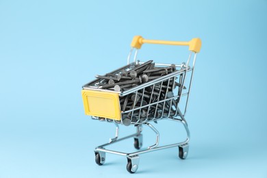 Metal nails in shopping cart on light blue background