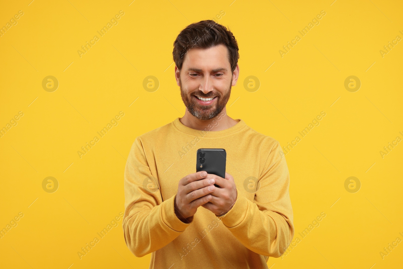 Photo of Handsome bearded using smartphone on orange background