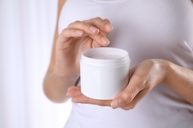 Photo of Woman with jar of moisturizing cream on light background, closeup