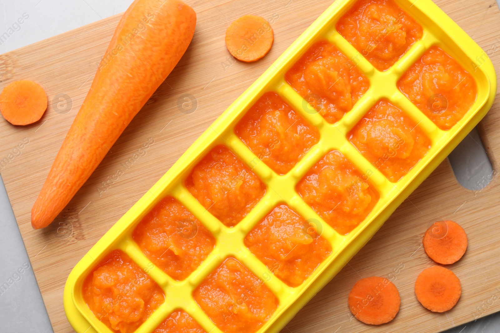 Photo of Carrot puree in ice cube tray on wooden board, flat lay. Ready for freezing