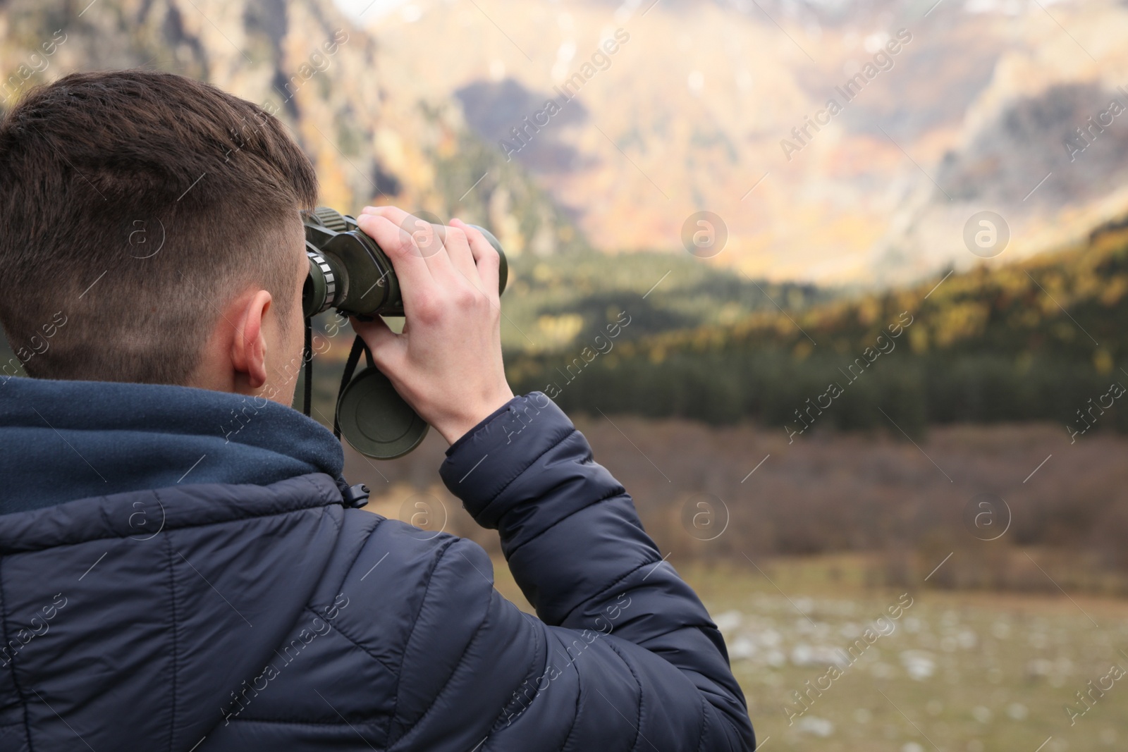 Photo of Boy looking through binoculars in beautiful mountains, back view. Space for text