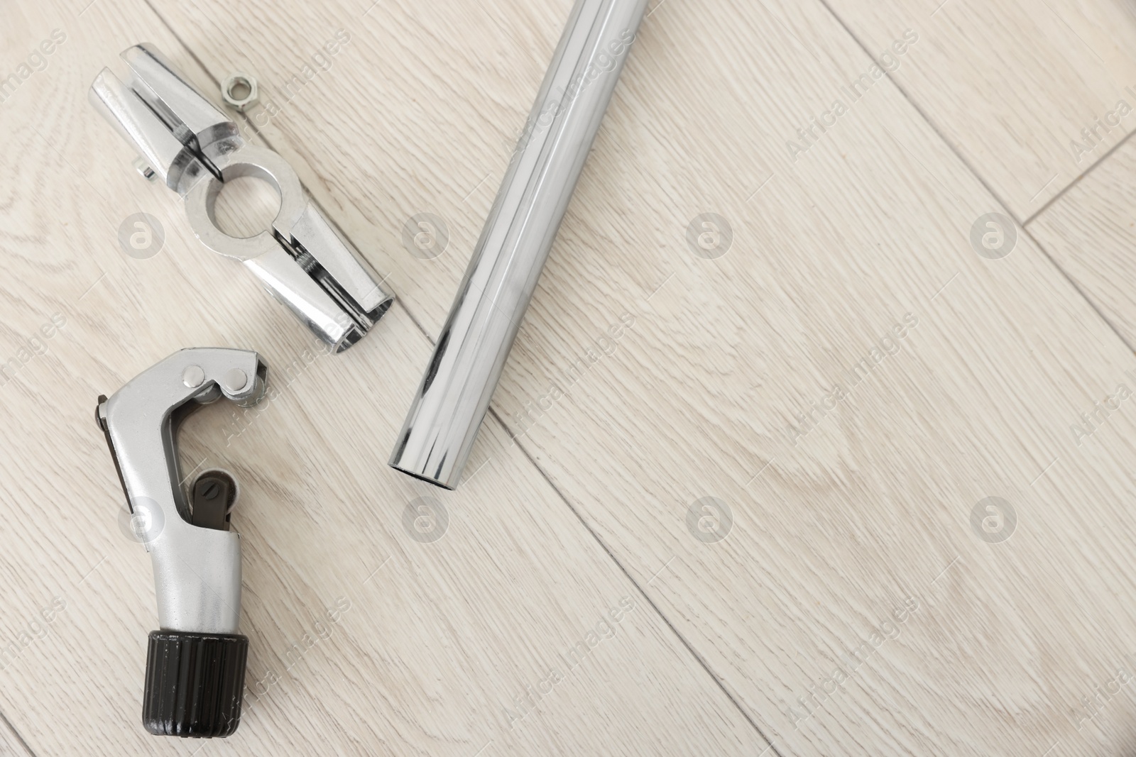 Photo of Modern metal wrench and pipe on wooden floor, top view. Space for text