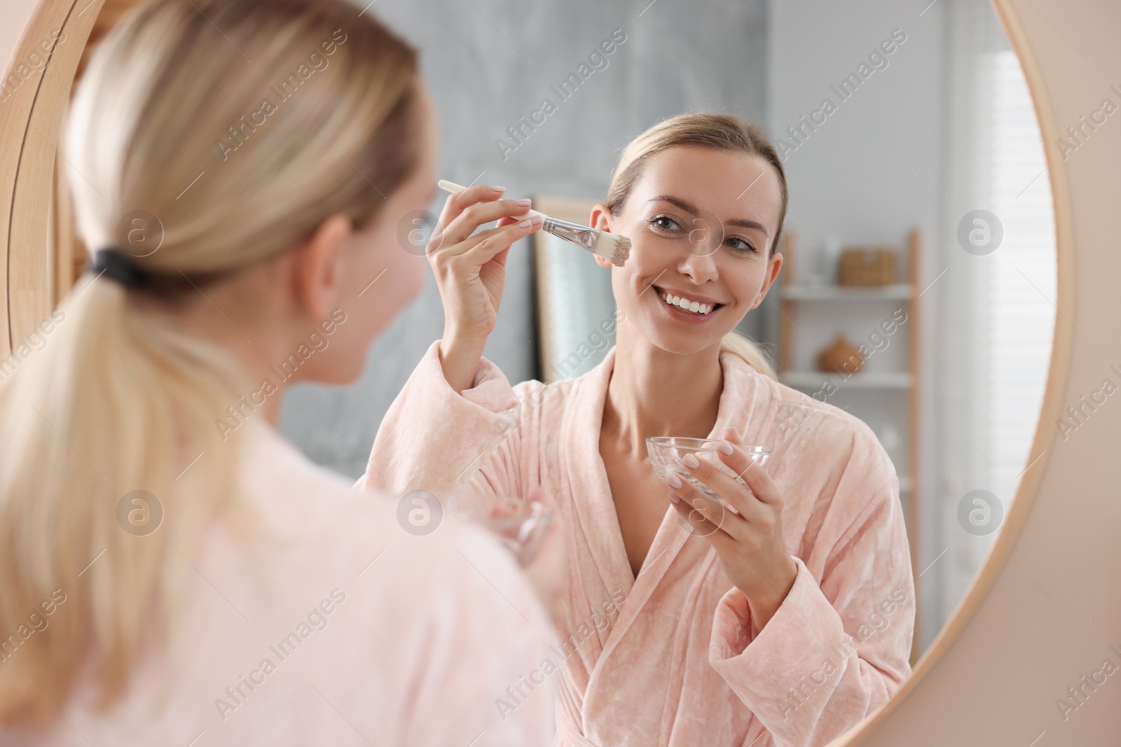 Photo of Woman applying face mask near mirror in bathroom. Spa treatments