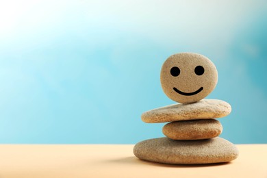 Photo of Stackstones with drawn happy face on beige table against light blue background, space for text. Zen concept