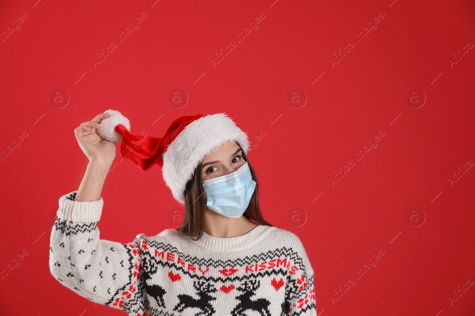 Photo of Pretty woman in Santa hat and medical mask on red background, space for text