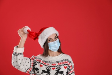 Pretty woman in Santa hat and medical mask on red background, space for text