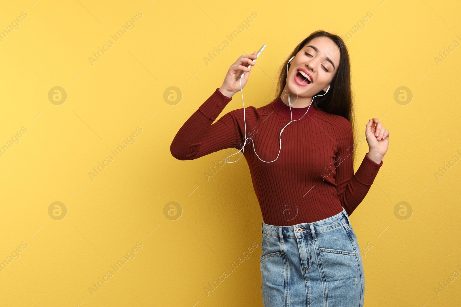 Photo of Young woman using phone for listening to music on color background